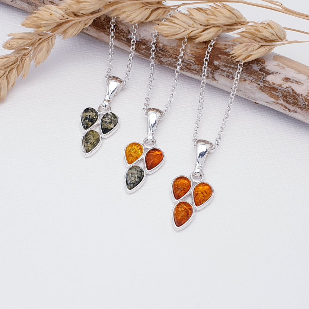 three pendants on sterling silver chains with three tear drop amber stones arranged in a triangle shape. the left is green amber, middle is mixed amber and the right is toffee amber