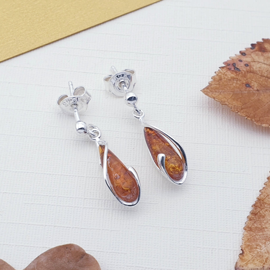 A pair of teardrop amber and sterling silver earrings with autumn foliage.