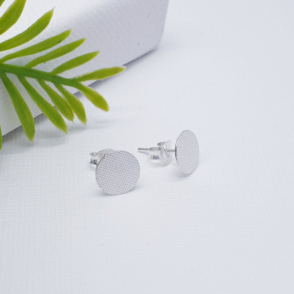 These contemporary studs feature a Silver textured effect and have a flat disk shape. Understated and simple, these earrings will complement any outfit and add a flash of glamour to your day.
