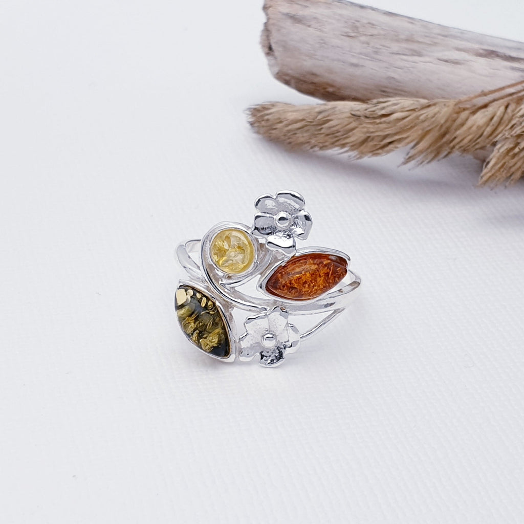 This ring features three Baltic Amber stones; two marquise shaped, in Toffee and green and one round yellow Amber stone. A Sterling Silver flower design decorates the top and bottom of the ring, finishing this design off beautifully.