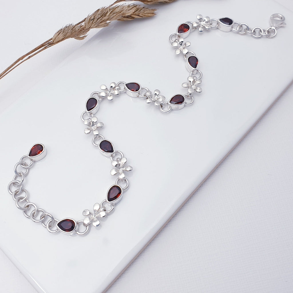 This bracelet features nine teardrop, tabletop cut, Garnet stones in simple settings, plus one more beautiful Garnet stone at the end of the extension chain. Decorative Sterling Silver flower links attach each stone to the next, creating a simple yet elegant bracelet. The extendable chain on the end gives you peace of mind when buying as a gift, as it can be worn in lengths 8" to 9.5", the perfect length for larger wrists.
