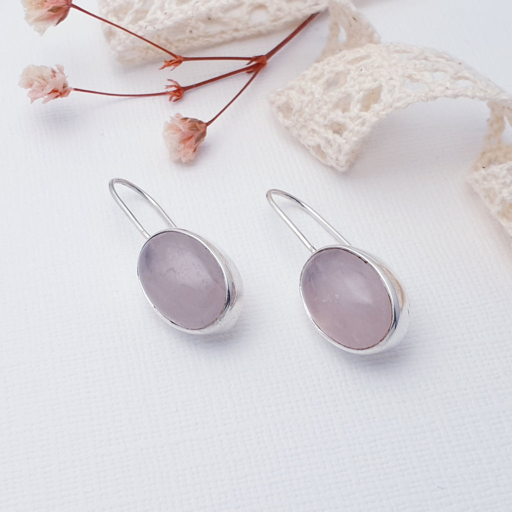 These earrings feature oval, cabochon, Rose Quartz stones in simple settings. The solid hook gives the design a fluid look while hugging the ear comfortably. Perfect for work but will transition effortlessly into play.