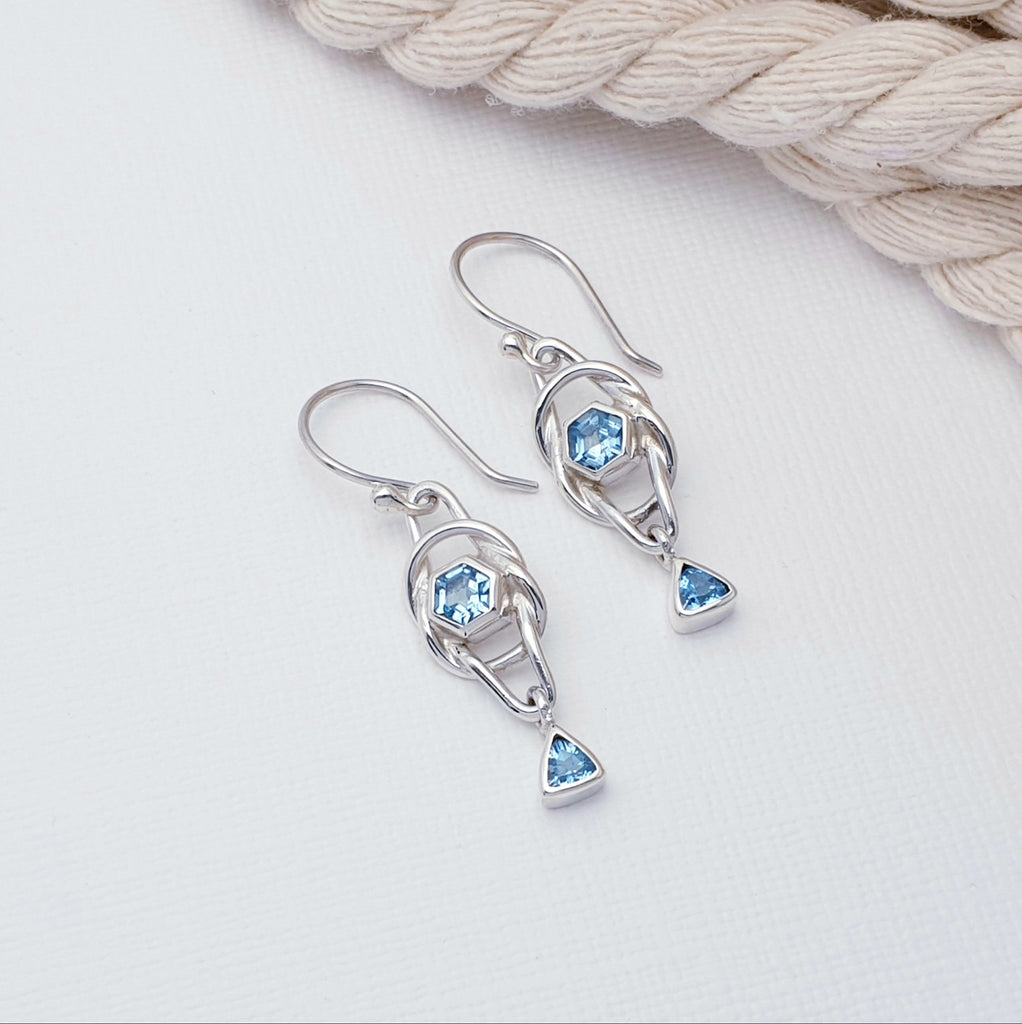 Each earring features a knot design hand worked in Sterling Silver. At the center of the knot there is a hexagon, tabletop cut, Blue Topaz stone. As a finishing touch a small triangle, tabletop Blue Topaz stone drops down from the bottom. A gorgeous design, these earrings are light on the ear, easy to wear and will soon become everyday favourites.