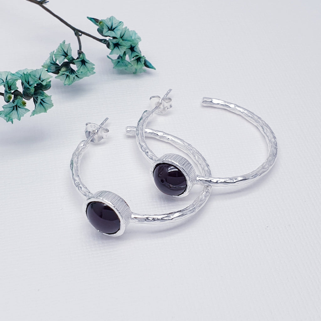 Each earring features a half hoop design with a beautiful, cabochon, Garnet stone in a  Sterling Silver setting. Each hoop has a Sterling Silver hammered effect creating that 'something a little different' we love at Silver Scene. The stud fixing makes these earrings extra secure so you don't need to worry about loosing them.
