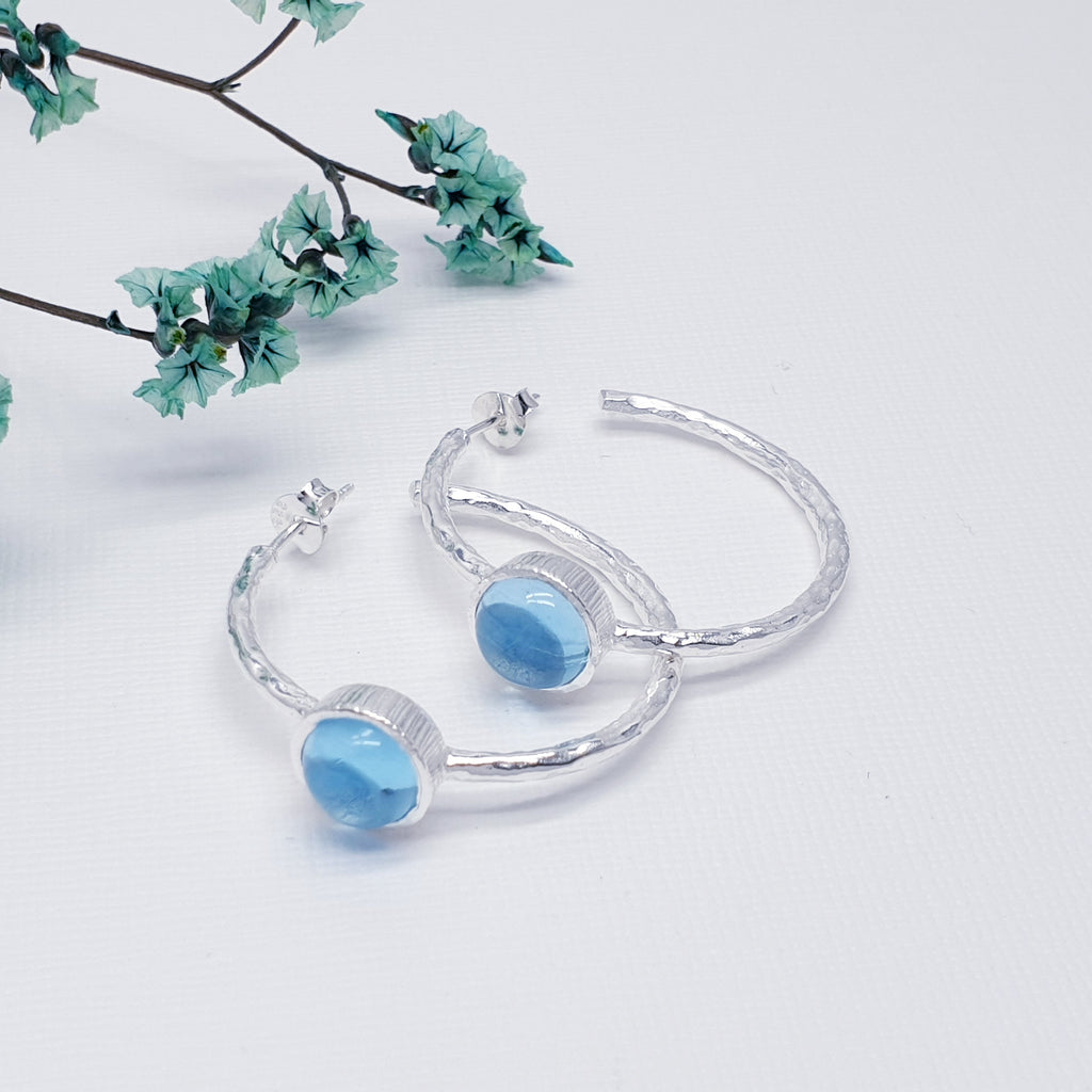 Each earring features a half hoop design with a beautiful, cabochon, Blue Topaz stone in a Sterling Silver setting. Each hoop has a Sterling Silver hammered effect creating that 'something a little different' we love at Silver Scene. The stud fixing makes these earrings extra secure so you don't need to worry about loosing them.