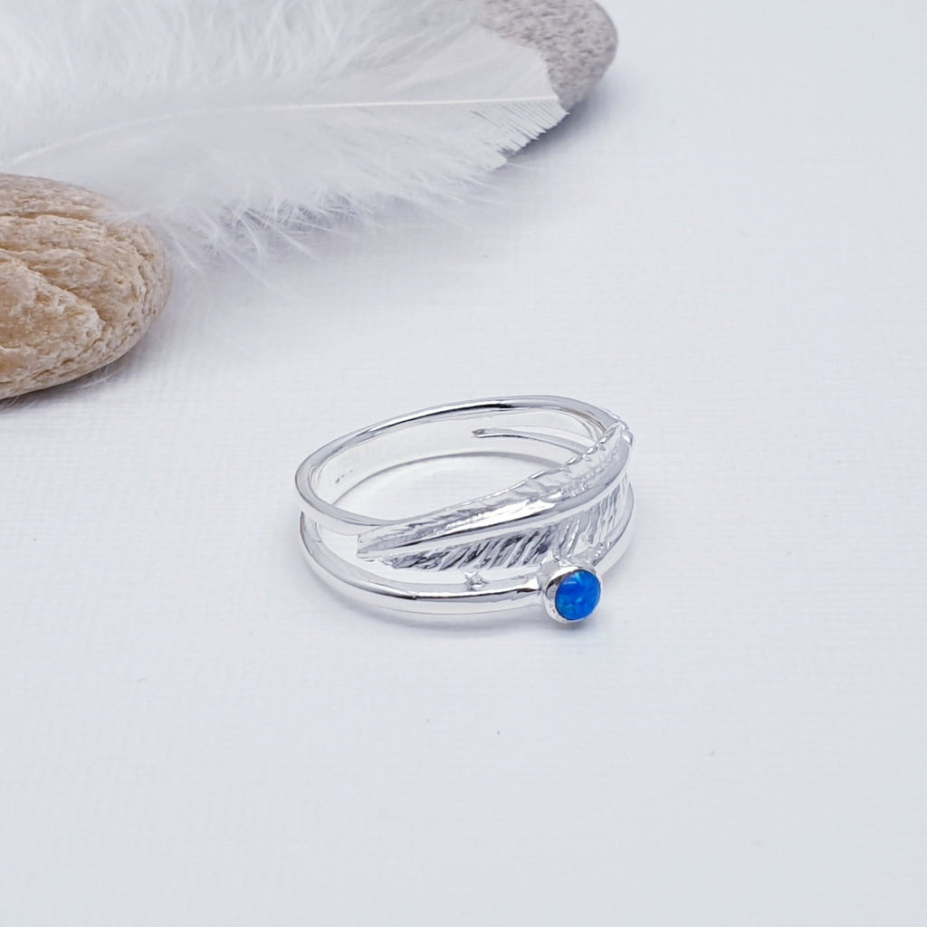 A beautiful design, this ring features a stunning cabochon, round, Reconstituted Opal stone in a simple setting. Above the stone is a gorgeous feather, with an 'icing sugar' finish and gorgeous detailing. Two silver bands are fused together at both ends creating an interesting design.