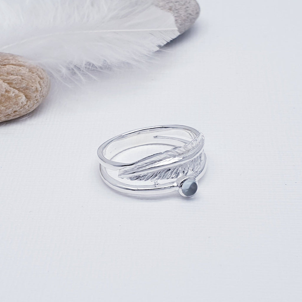 A beautiful design, this ring features a stunning cabochon, round, Blue Topaz stone in a simple setting. Above the stone is a gorgeous feather, with an 'icing sugar' finish and gorgeous detailing. Two silver bands are fused together at both ends creating an interesting design.