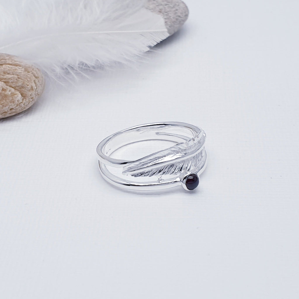 A beautiful design, this ring features a stunning cabochon, round, Garnet stone in a simple setting. Above the stone is a gorgeous feather, with an 'icing sugar' finish and gorgeous detailing. Two silver bands are fused together at both ends creating an interesting design.