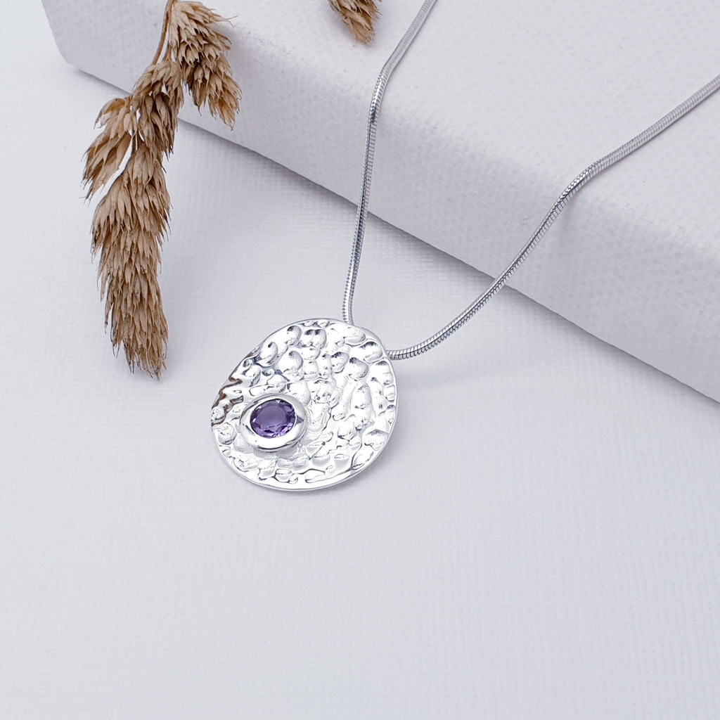 Our Amethyst Sterling Silver Hammered Disk Pendant (chain not included) is so cute and would be perfect for everyday wear.  This stunning pendant features a small, cabochon Amethyst sitting off-center on a beautiful, hammered Sterling Silver disk. This textured effect creates a stunning, reflective surface which catches the light as you move. 