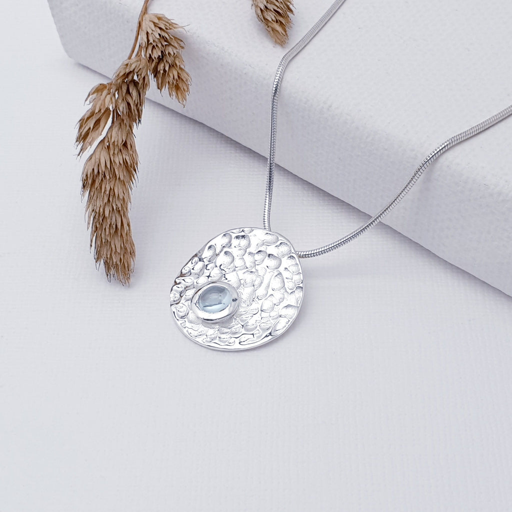Our Blue Topaz Sterling Silver Hammered Disk Pendant (chain not included) is so cute and would be perfect for everyday wear.  This stunning pendant features a small, cabochon Blue Topaz sitting off-center on a beautiful, hammered Sterling Silver disk. 