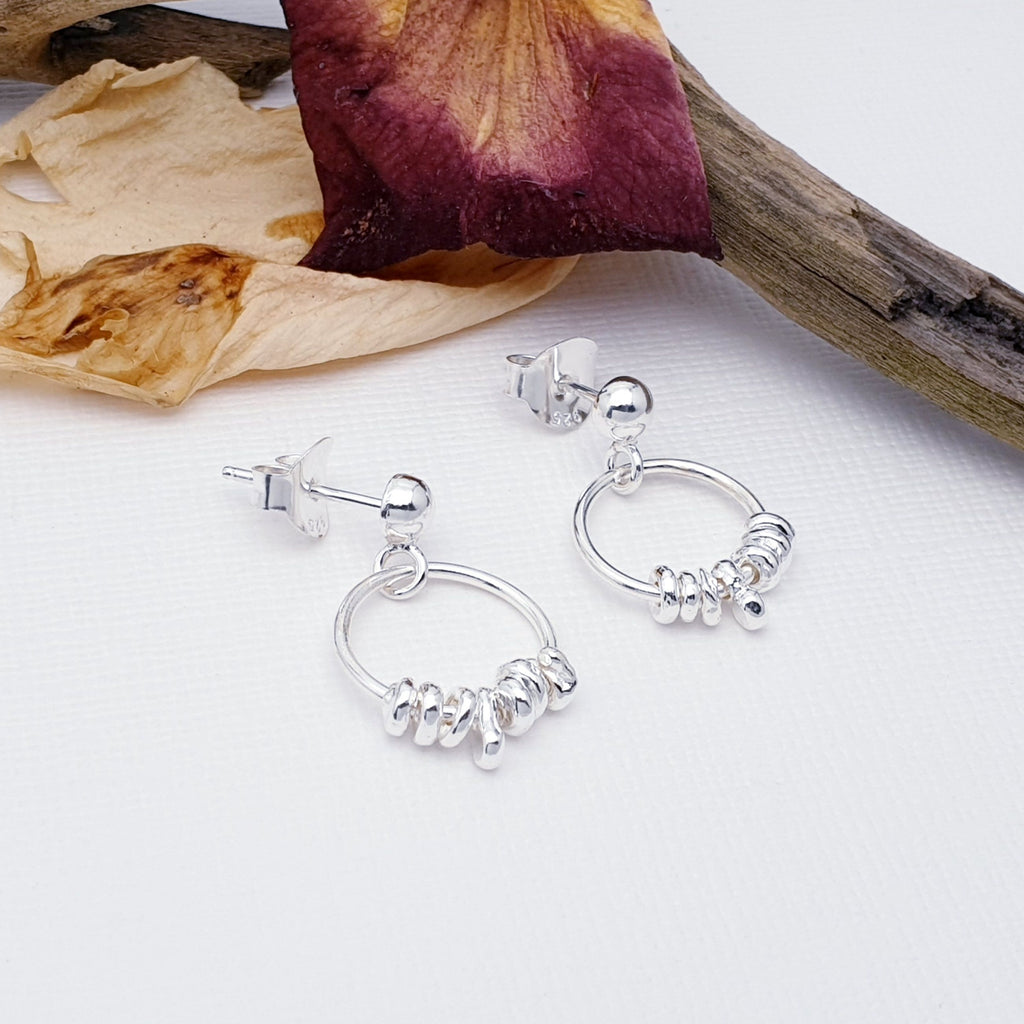 Each Sterling Silver stud earring features small silver circles that delicately hang from the bottom of a small hoop. A simple yet unusual design, these are perfect for work or play.