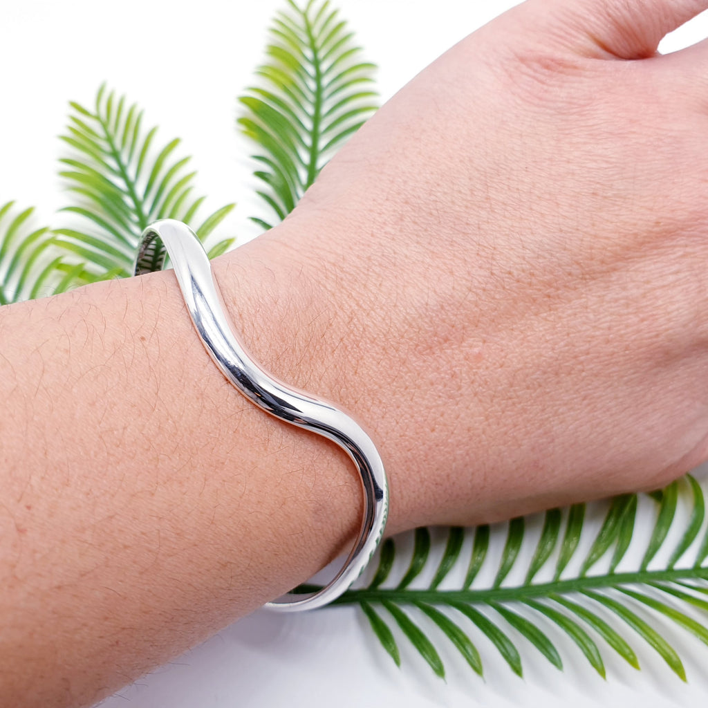 sterling silver wavey cuff bracelet on a wrist with foliage background