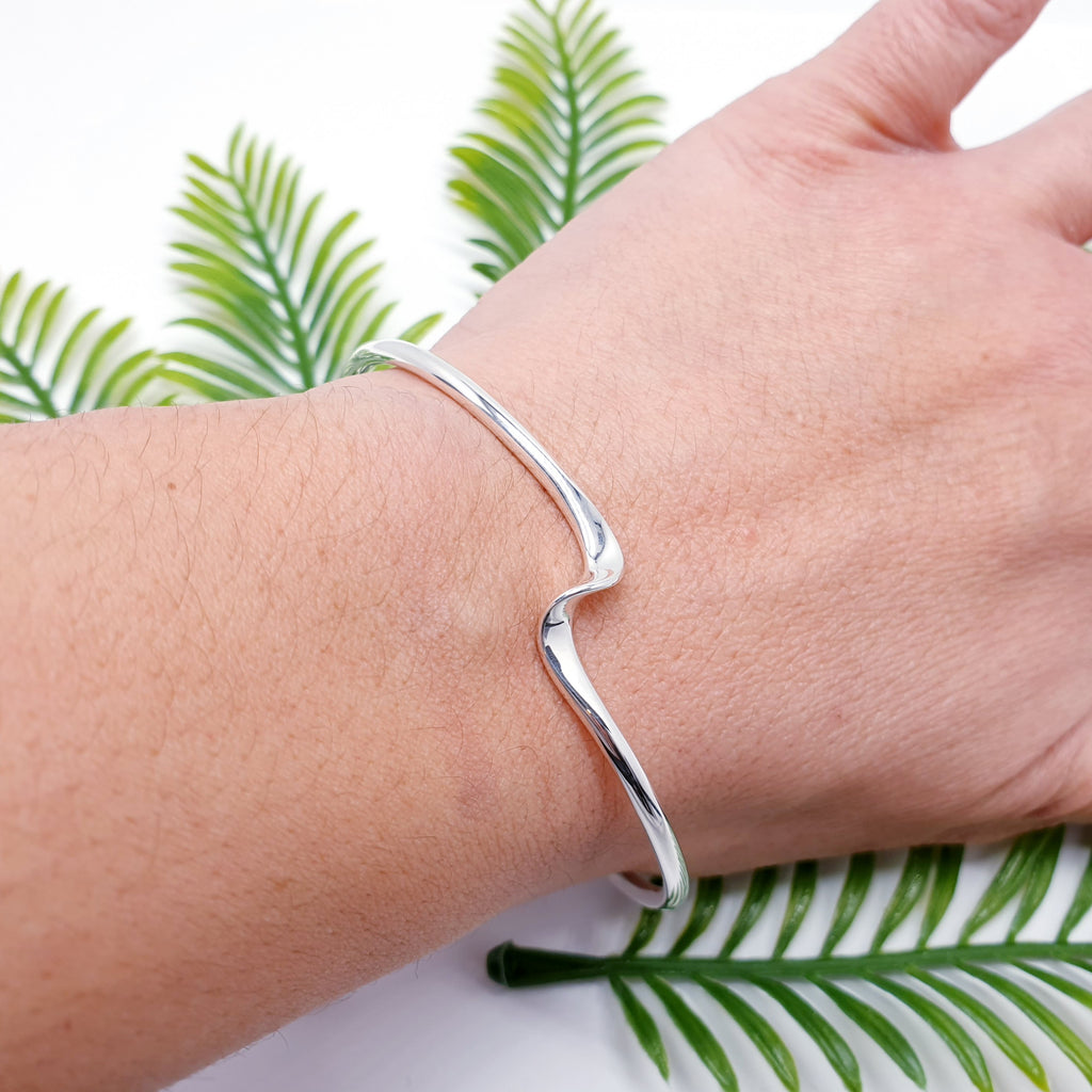 sterling silver wave shaped bangle cuff on wrist with green foliage background