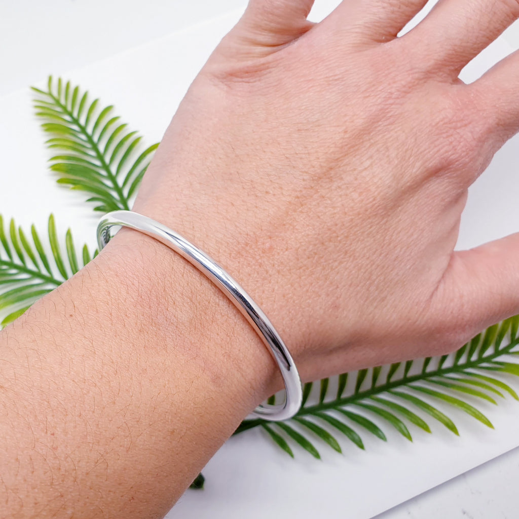 simple sterling silver round band bangle on wrist with foliage background