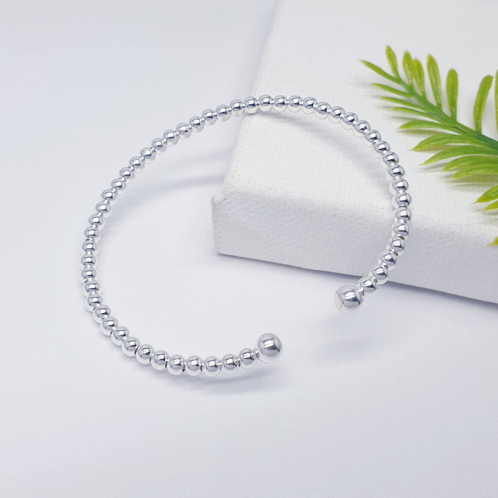 Silver multi ball cuff bracelet displayed against a white background with green foliage in the background