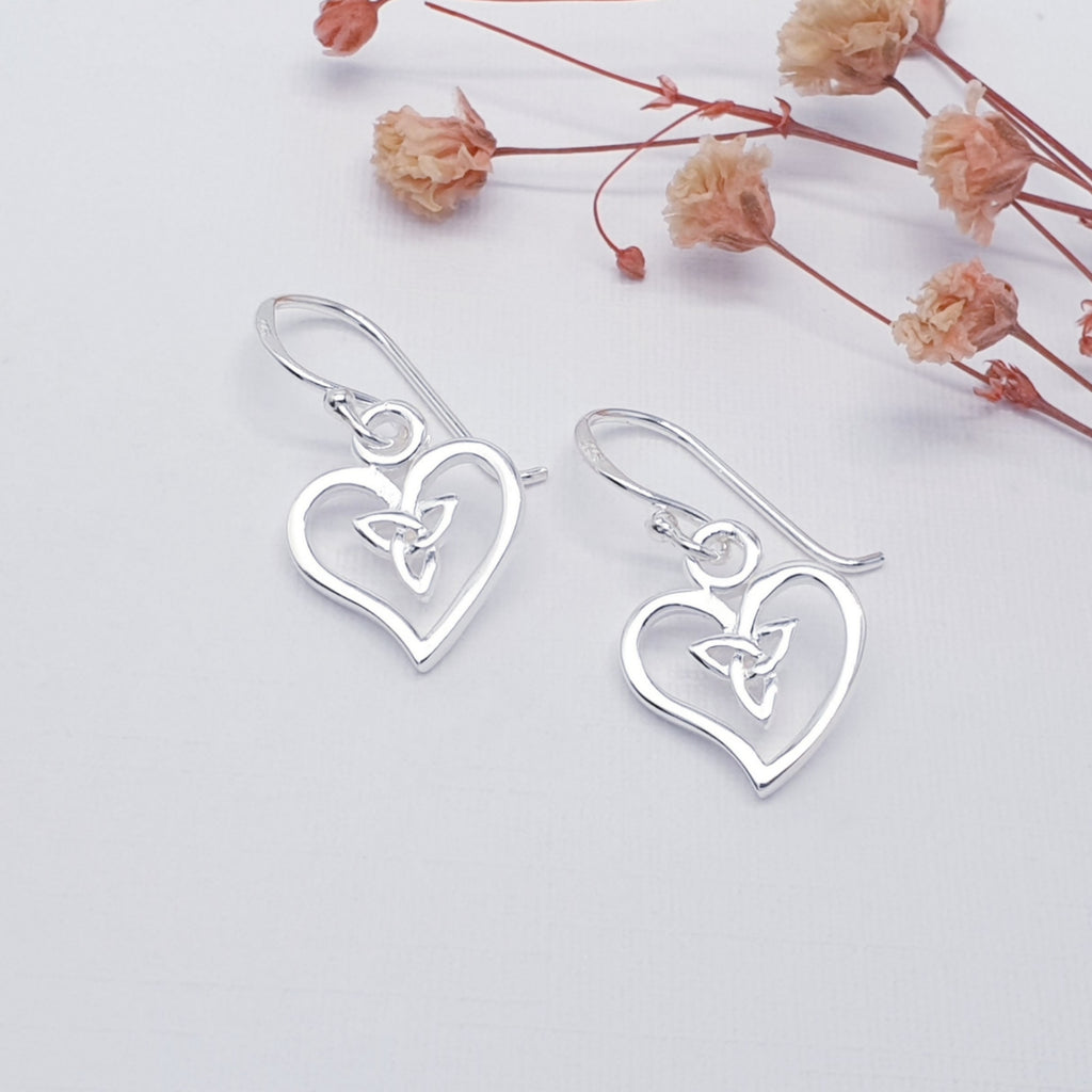 handmade heart and celtic knot sterling silver earrings displayed on a white background with pink flowers as decorations