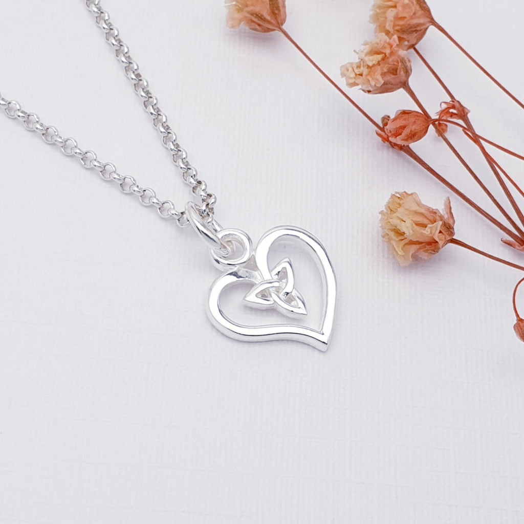 handmade heart and celtic knot sterling silver pendant displayed on a white background with pink flowers as decorations