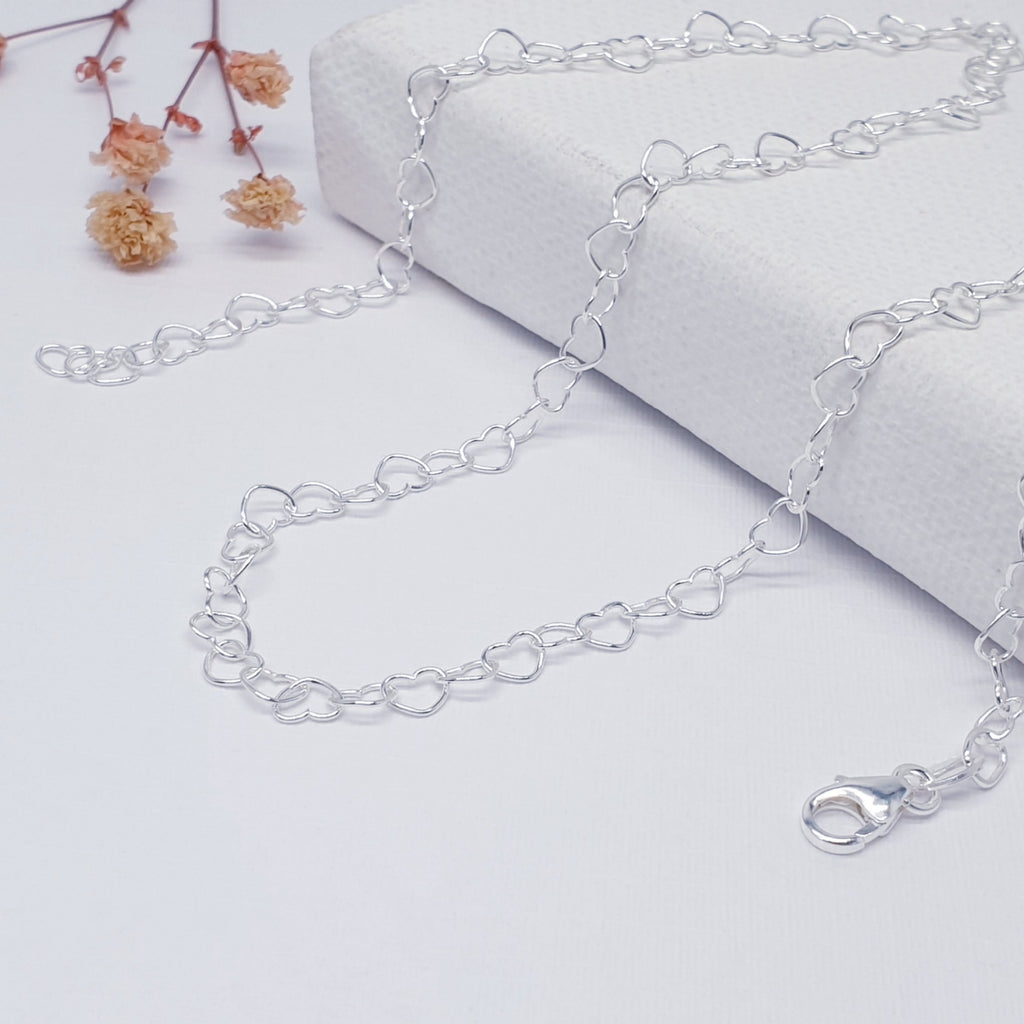 handmade delicate sterling silver heart chain necklace displayed on a white background with pink flowers as decoration
