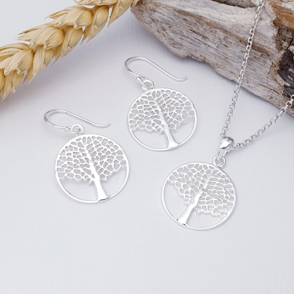 Sterling silver tree of life dangle earrings with hooks. Next to a sterling silver tree of life pendant. On a white background with wheat and bark as decorations.