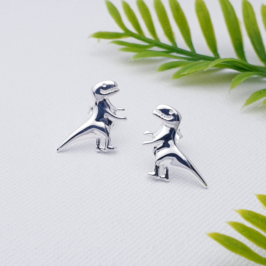 Sterling Silver T-Rex Studs on a white background with green foliage