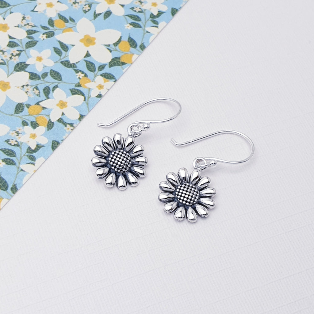 Sterling silver sunflower earrings on a white background with a floral piece of card in the left hand corner.