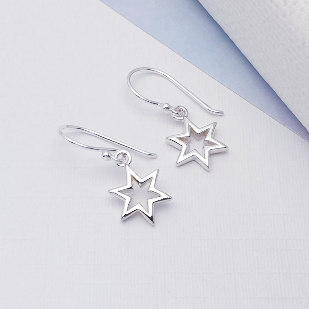 Small sterling silver star earrings, with a hollow middle. On a white background with a hint of blue in the right hand top corner.