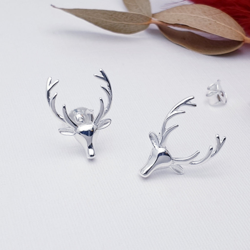 Reindeer head stud earrings on a white background, with leaves in the background