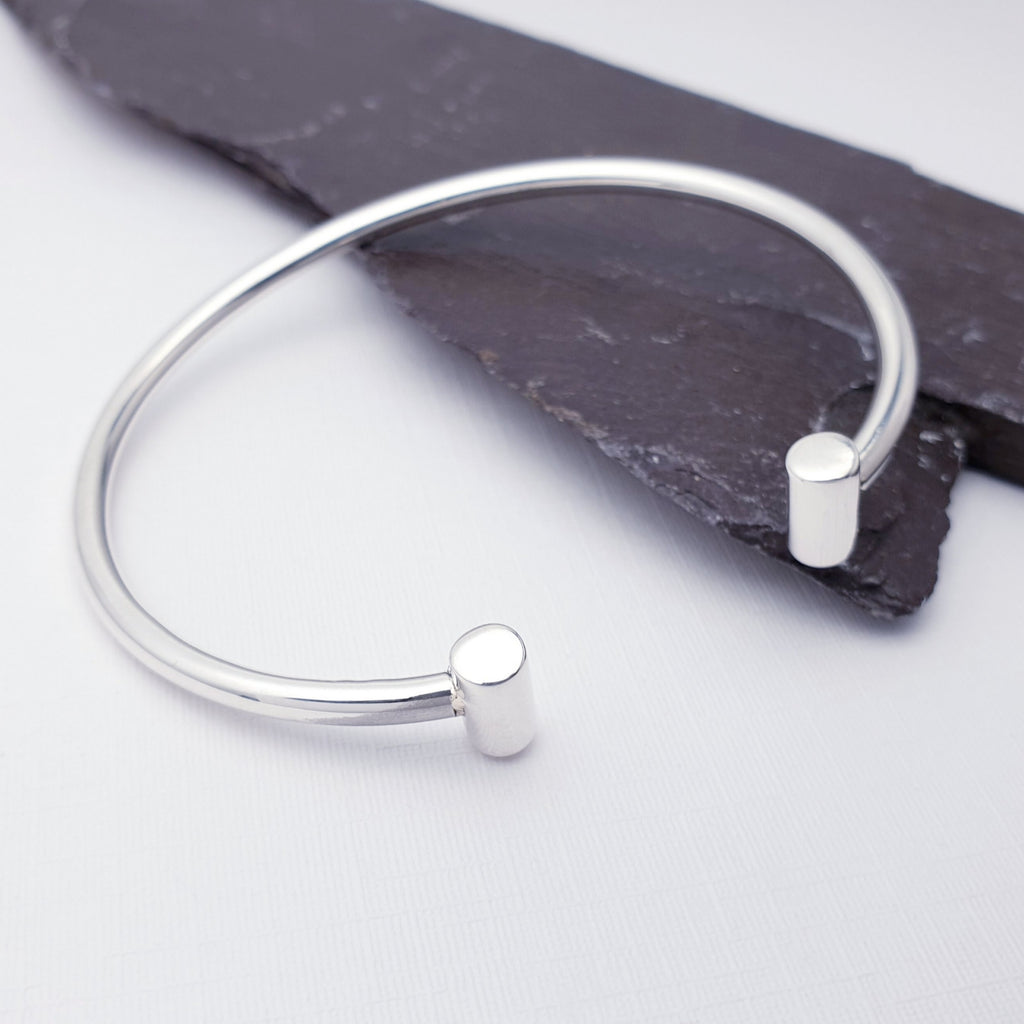 T Bar cuff bracelet on a white background with a piece of slate on the right hand side. The cuff is half on the piece of slate, raising it slightly.