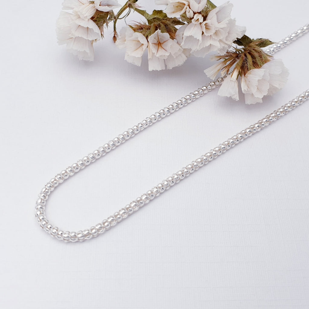 Popcorn chain on a white background with white foliage in the top left corner