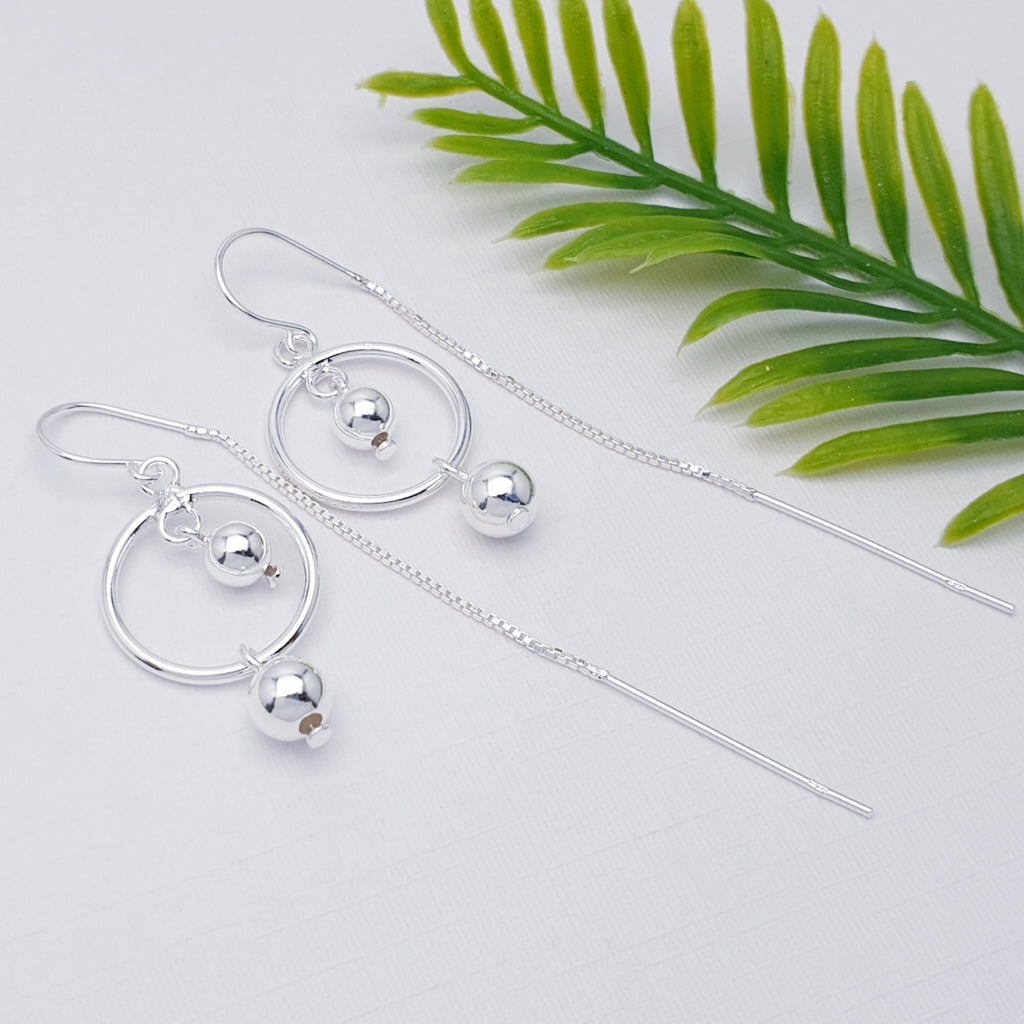 Sterling Silver Ring and Ball Pull Through Earrings on a white background with green leaves on the right hand side