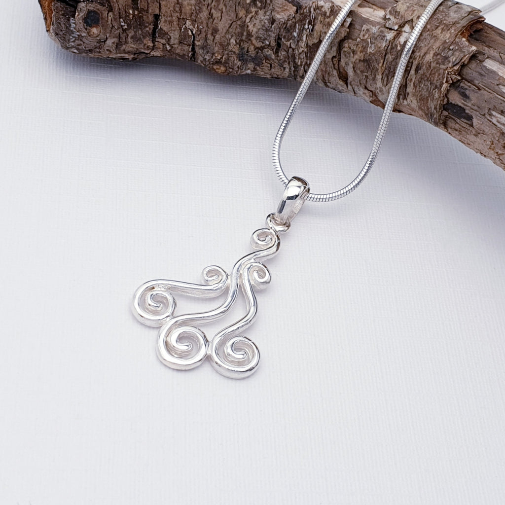 Sterling Silver Spiral Pendant on a white background, paired with a fine snake chain draped across some bark in the top half of the image