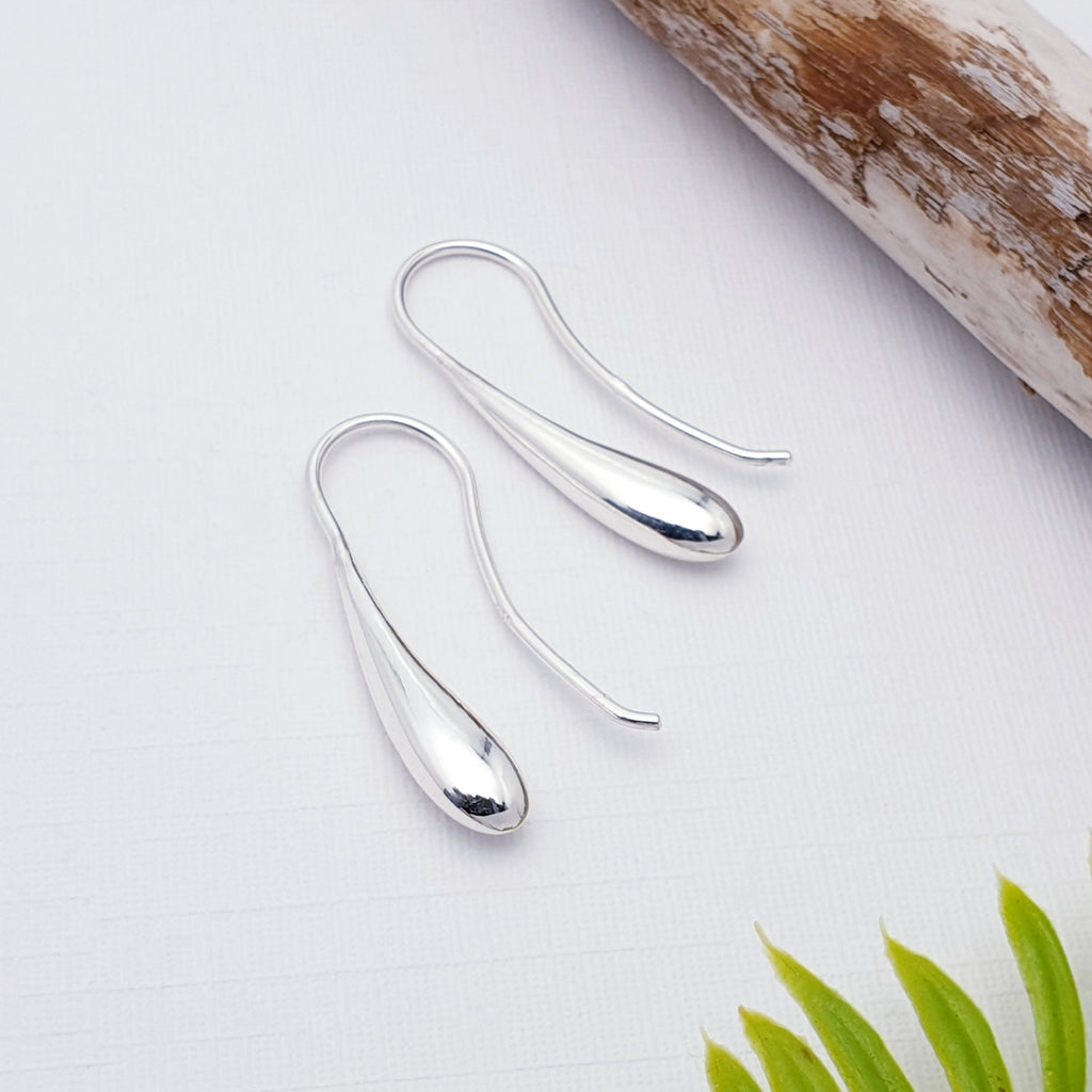 Sterling Silver Droplet Earrings on a white background with wood in the top right corner and piece of leaf in the bottom right