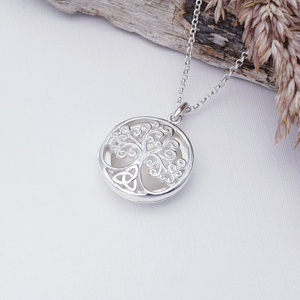 Sterling Silver Tree Of Life Locket on a white background with drift wood and barley in the top right corner of the image