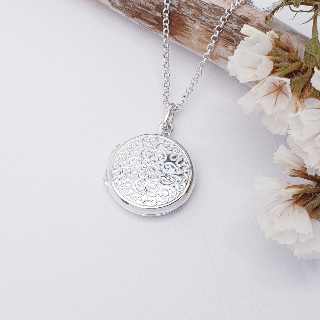 Sterling Silver Round Floral Locket on a white background with wood and white flowers in the top right corner