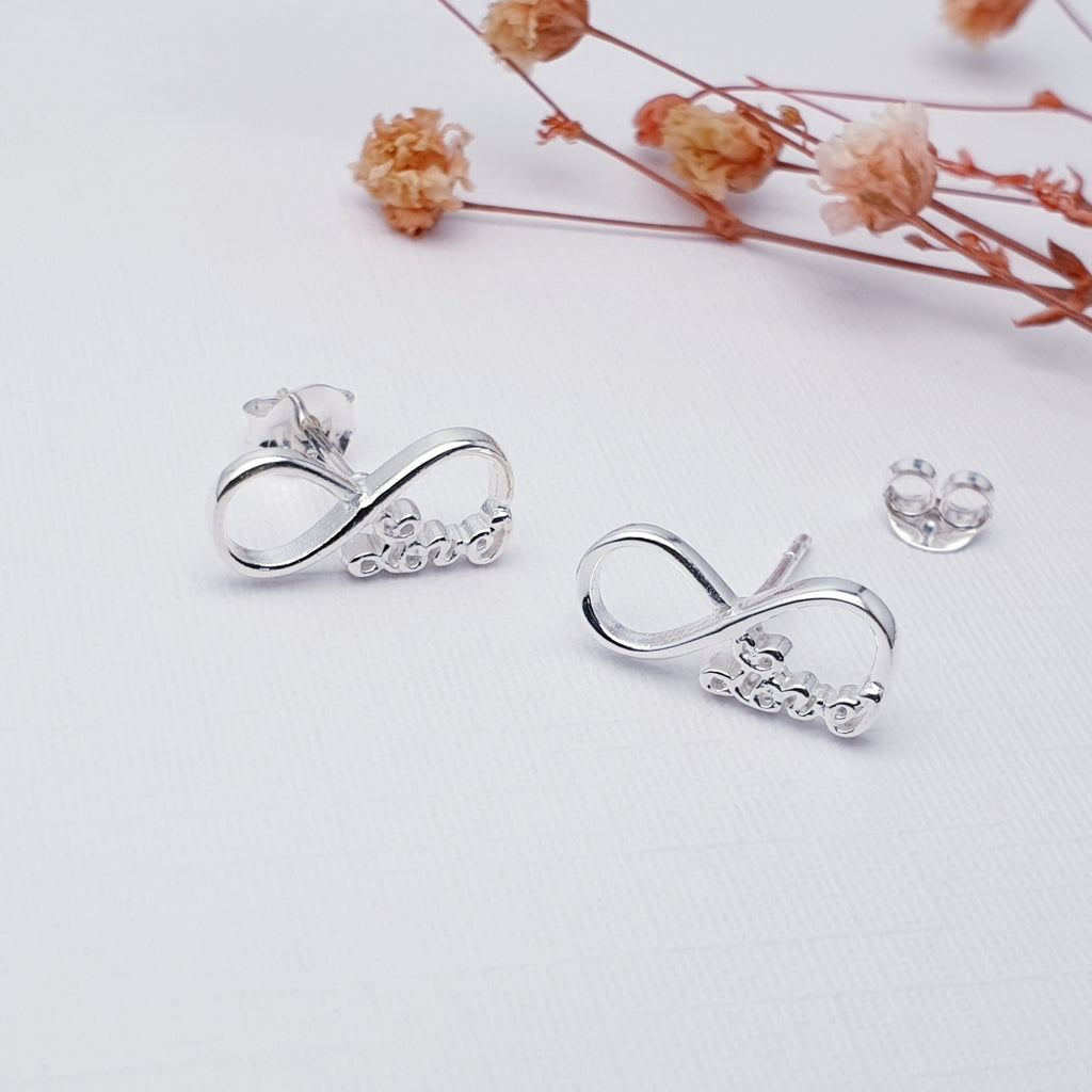 Our Infinity Love studs displayed on white background with pink flowers as decorations