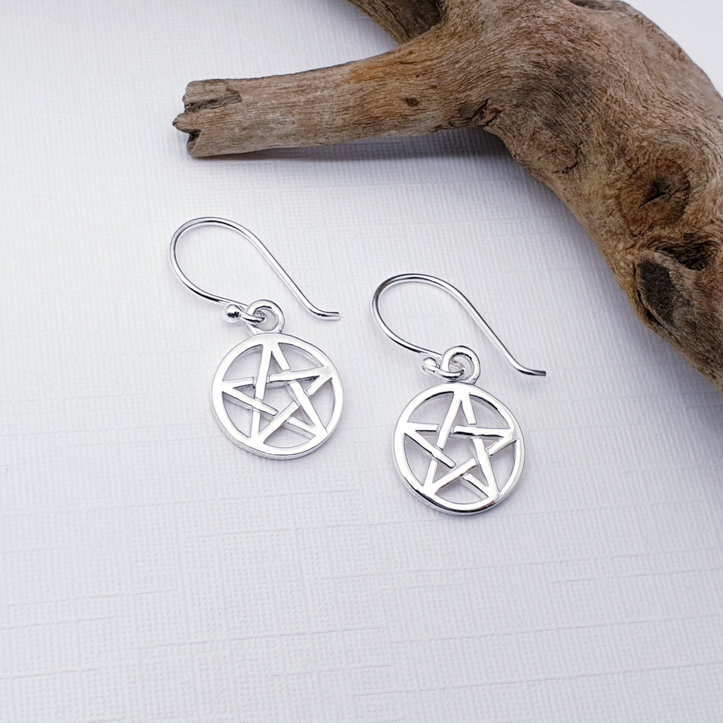 Our Sterling Silver Pentagram earrings displayed against a white background with driftwood as decoration