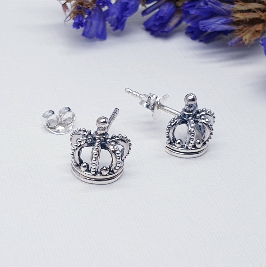 Our Sterling Silver Royal studs displayed against a white background with purple flowers in the background as decoration
