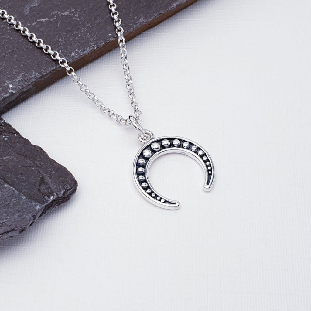 Our sterling silver inverted crescent moon pendant on a fine belcher chain, displayed on a white background with slate as decoration