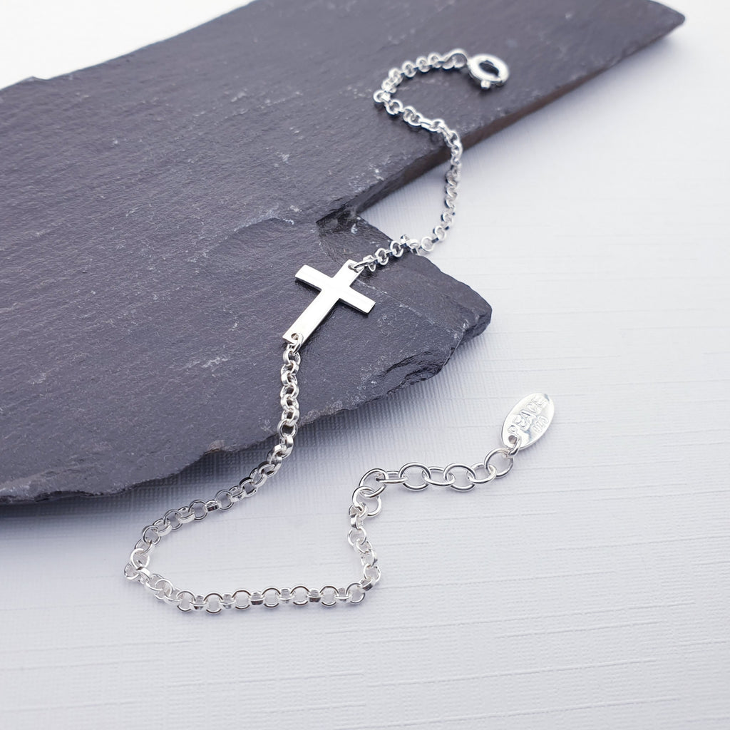 Our sterling silver cross bracelet draped over a piece of slate and displayed on a white background
