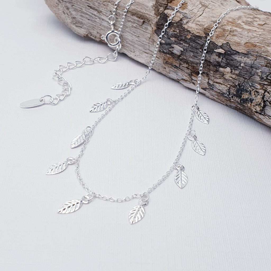 Our sterling silver falling leaves necklace draped over a piece of drift wood and displayed on a white background
