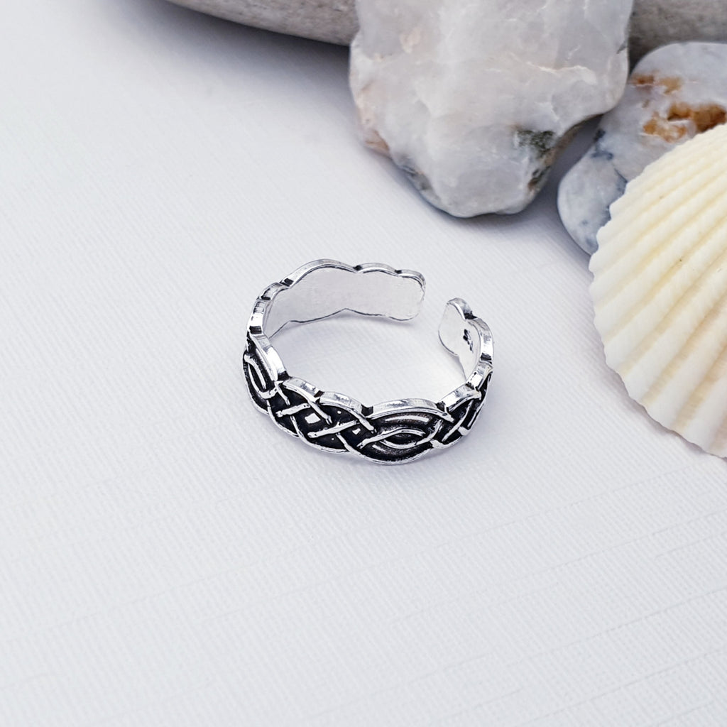 Our Sterling Silver Oxidised Celtic Toe Ring displayed on a white background with stones and shells as decoration in the background
