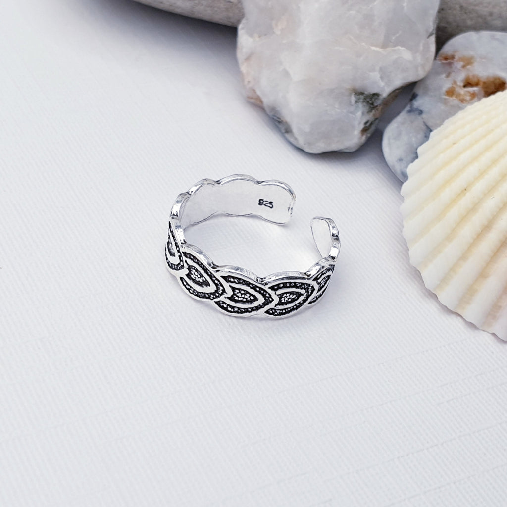 Our sterling silver celtic heart ring displayed on a white background with stones and shells as decorations