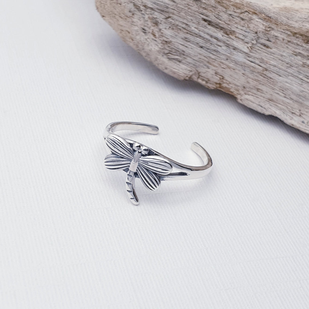 Our sterling silver dragonfly toe ring displayed on a white background with driftwood as decoration