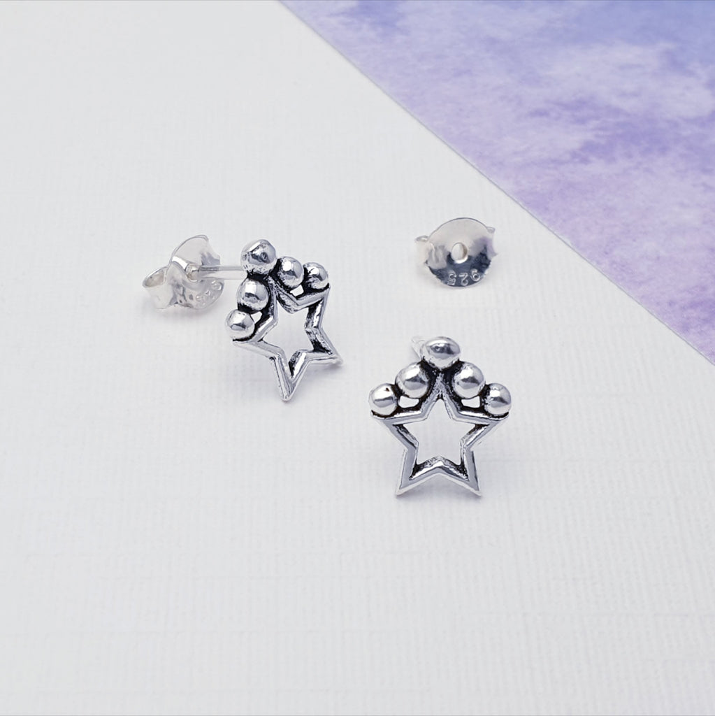 Our sterling silver oxidised star studs displayed against white with purple card in the background as decoration