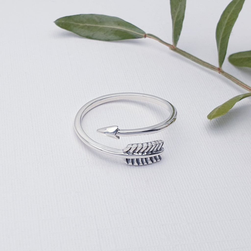 Our sterling silver feather arrow adjustable ring displayed on a white background with leaves as decoration