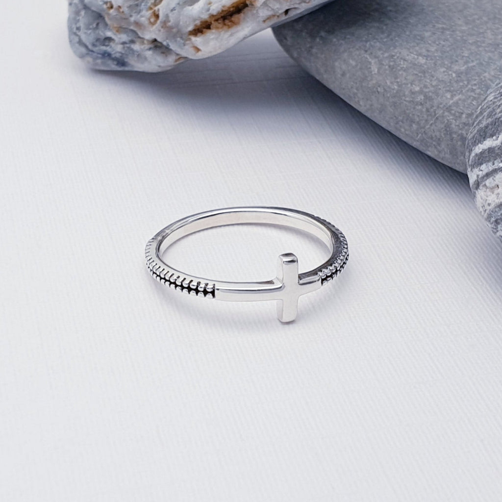 Our sterling silver oxidised cross ring displayed on white with rocks in the background as decoration