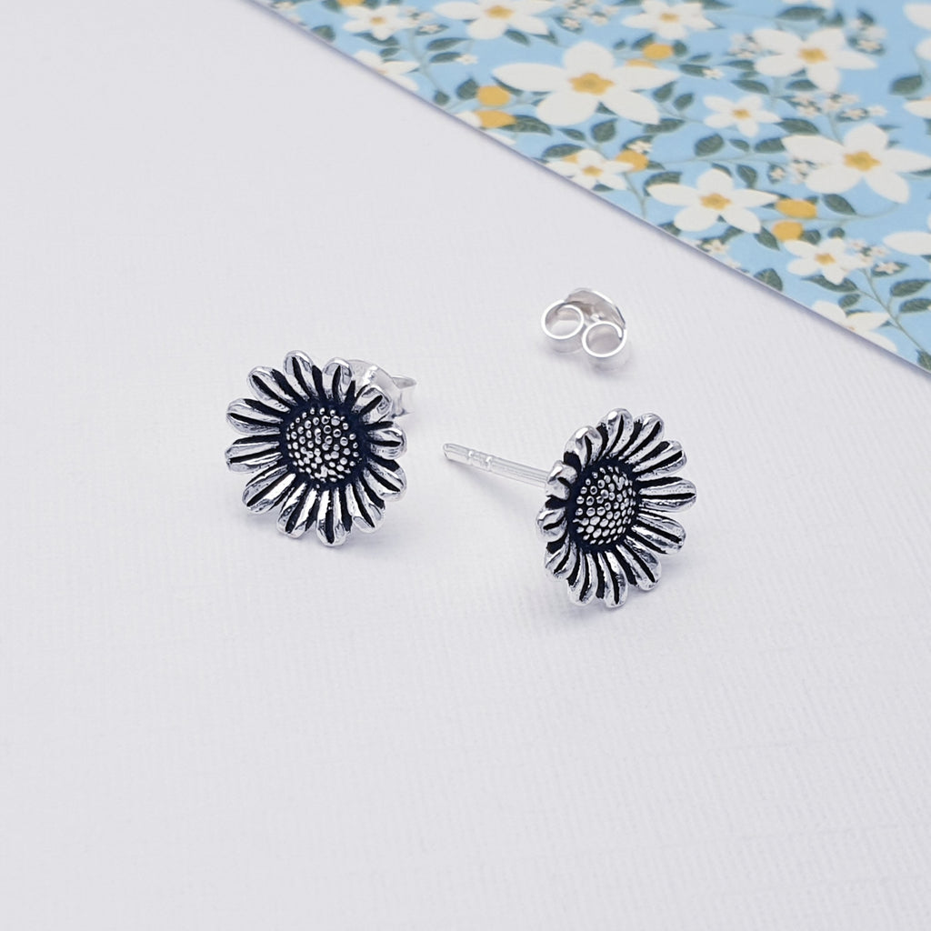 Our sterling silver sunflower studs displayed against white with a flowery piece of card in the background as decoration