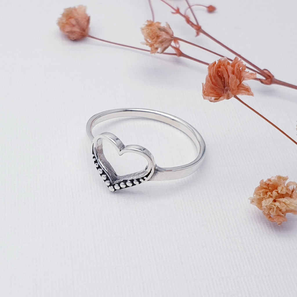 Silver heart-shaped ring on a white background with dried flowers