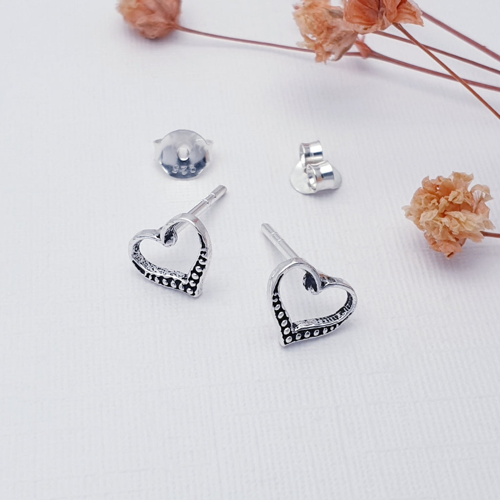 Heart-shaped silver studs on a light background with dried flowers.