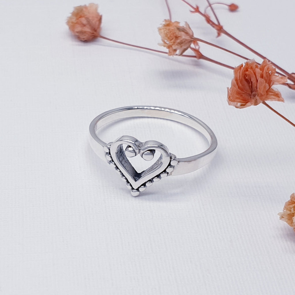 Silver heart-shaped ring on a white background with dried flowers.